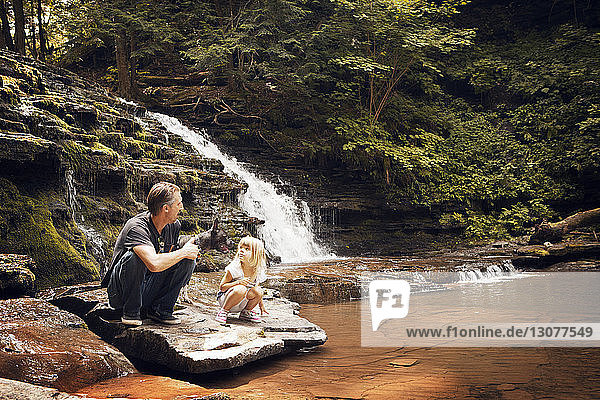 Grossvater und Enkelin mit Hund kauern auf Felsen am Seeufer