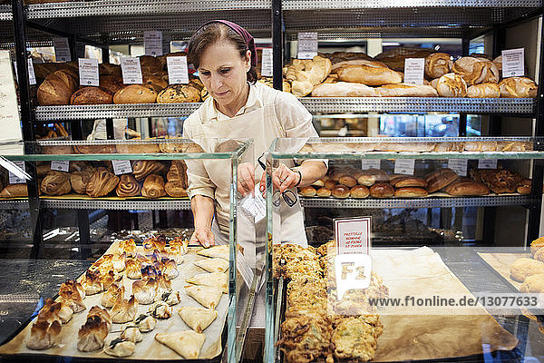 Chef arranging baked food in display cabinet at bakery shop