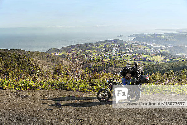 Älteres Ehepaar mit Blick auf die Berge  während es mit dem Motorrad auf der Straße steht