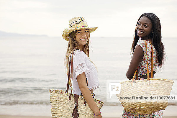 Side view portrait of happy female friends standing on shore at beach