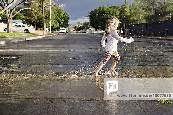 Seitenansicht eines Mädchens  das während der Regenzeit auf einer nassen Straße läuft