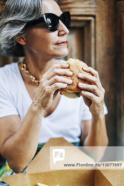 Frau mit Sonnenbrille schaut weg  während sie Burger hält