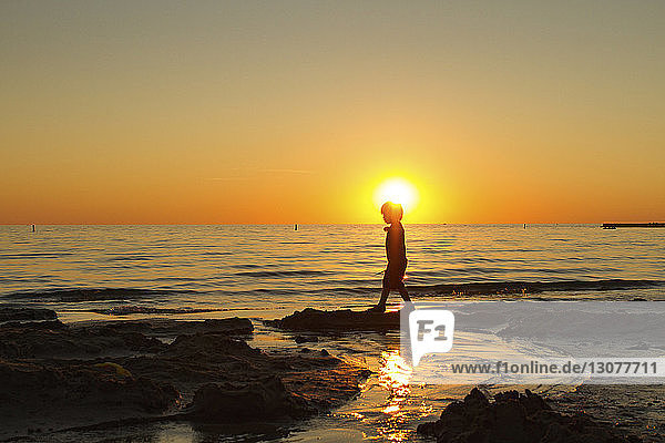 Seitenansicht eines Silhouettenjungen  der bei Sonnenuntergang am Strand spazieren geht