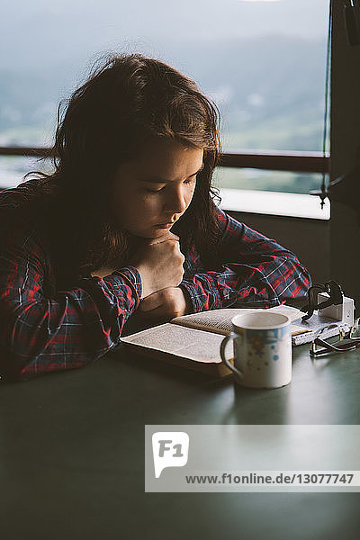 Young woman reading book with coffee cup at table
