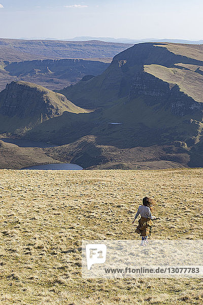 Rear view of woman walking on field against mountains
