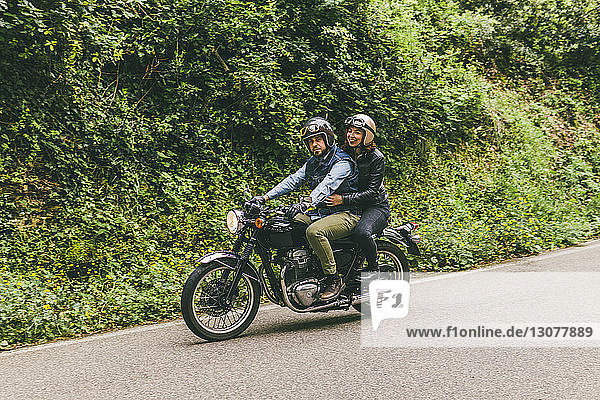 Paar fährt Motorrad auf der Straße zwischen Bäumen im Wald