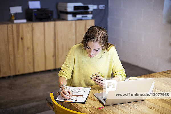 Businesswoman eating sandwich while working at table in office