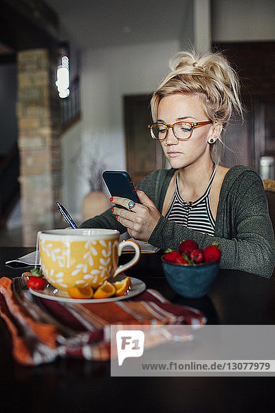 Woman using smart phone while sitting at breakfast table