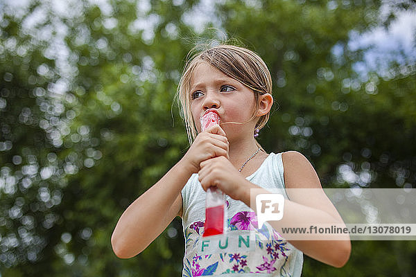 Niedrigwinkelansicht eines Mädchens  das beim Essen von aromatisiertem Eis im Park wegschaut