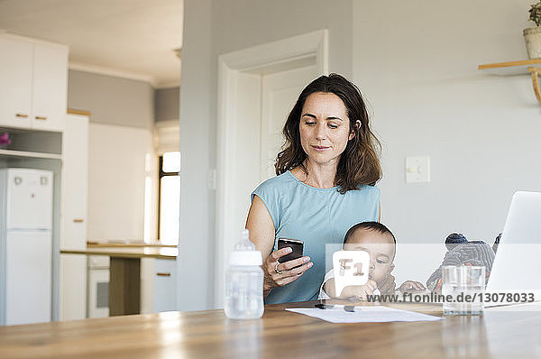 Frau benutzt Smartphone  während sie mit ihrem Sohn zu Hause sitzt