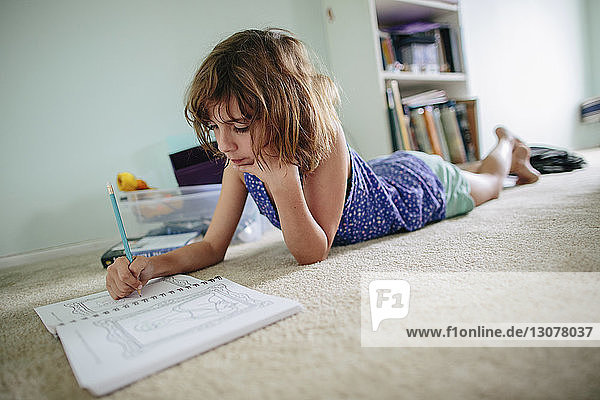 Mädchen macht Hausaufgaben  während sie zu Hause auf dem Boden liegt