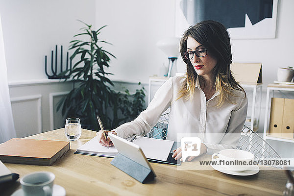 Businesswoman writing while sitting at desk in office