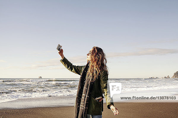 Seitenansicht einer Frau  die mit einem Smartphone am Strand fotografiert