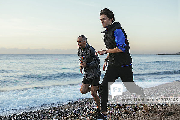 Father and son jogging together at beach against sky