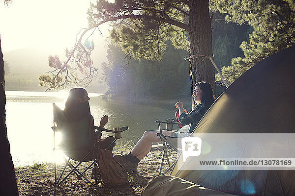 Female friends relaxing at campsite by lake during sunny day