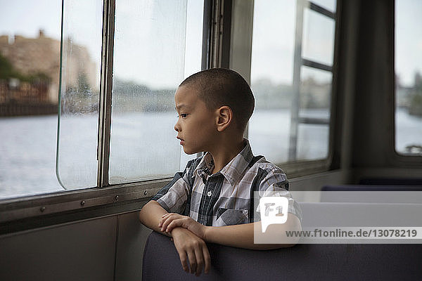 Thoughtful boy looking through window while traveling in ferry