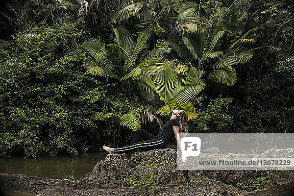 Seitenansicht einer Frau  die sich auf Felsen am Seeufer im El Yunque National Forest entspannt