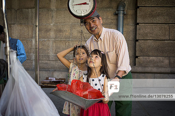 Enkelinnen mit Großvater-Gewichtssack auf Waage am Marktstand