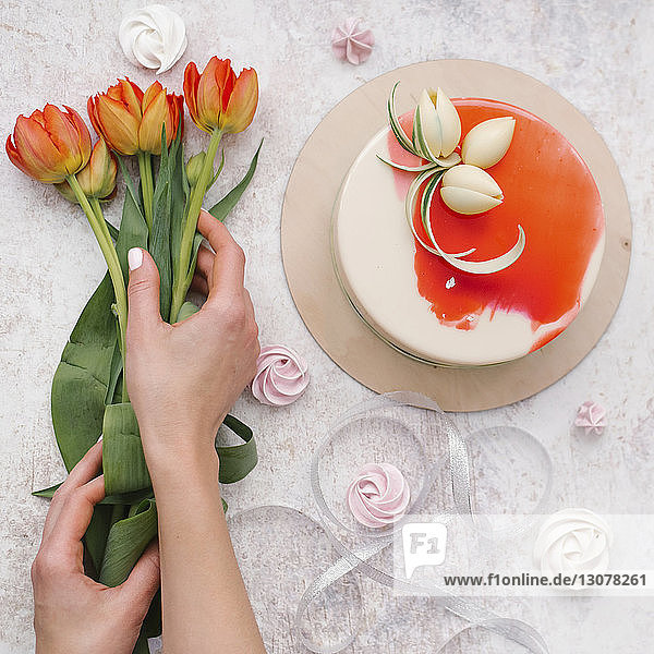 Geschnittene Hände einer Frau  die zu Hause Blumen nach Kuchen auf dem Tisch arrangiert