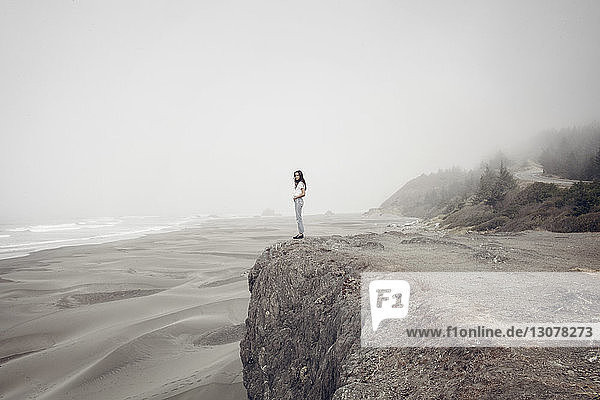 Seitenansicht einer Frau  die bei nebligem Wetter auf einer Klippe am Strand steht