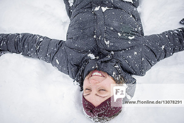 Happy woman with arms outstretched lying on snow covered field