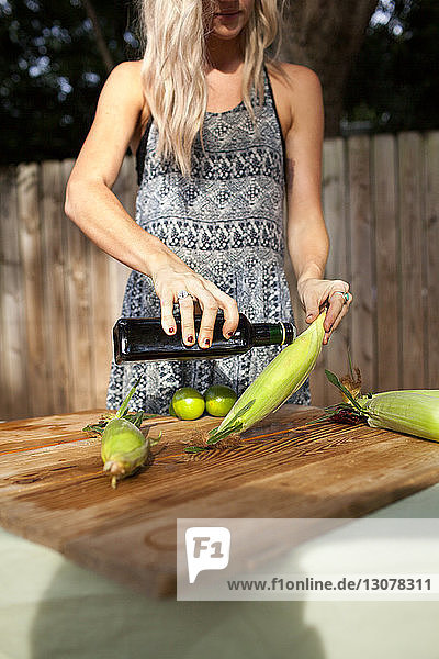 Midsection of woman pouring olive oil on corn