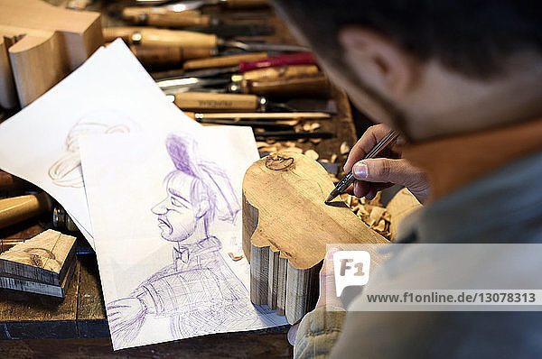 Hochwinkelansicht eines Handwerkers  der in der Werkstatt auf Skulptur zeichnet