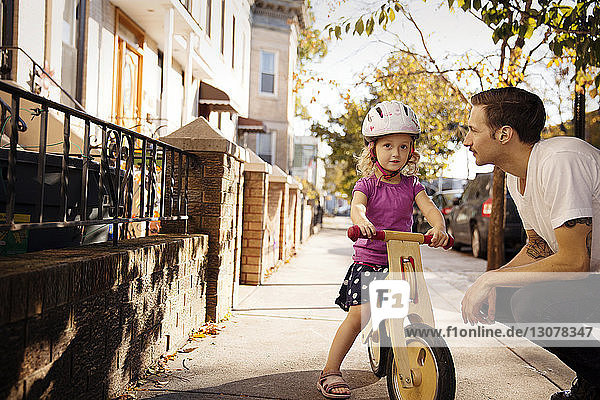 Vater sieht Tochter an  die auf dem Fahrrad vor Gebäuden in der Stadt sitzt