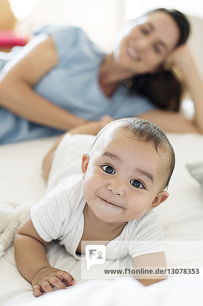 Mother looking at baby boy while lying on bed at home