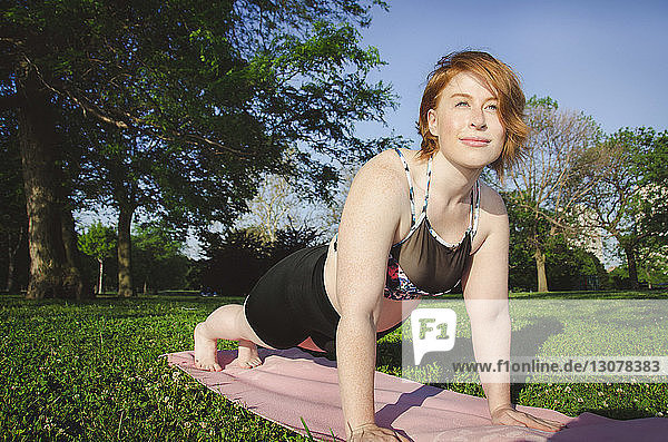 Frau schaut weg  während sie auf einer Übungsmatte im Park Yoga übt