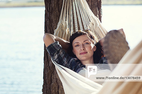 Porträt einer Frau  die sich am Seeufer auf einer Hängematte am Baum entspannt