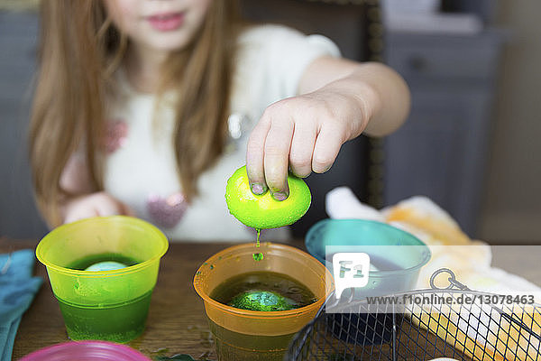 Mitschnitt eines Mädchens  das sein Osterei zu Hause auf dem Tisch in gefärbtes Wasser taucht