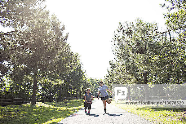 Mother and daughter stretching legs while exercising on footpath at park during sunny day