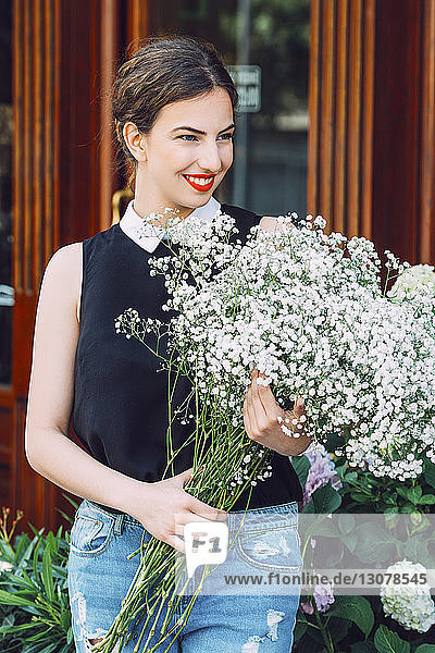 Lächelnde Floristin hält weißen Blumenstrauß vor Blumenladen