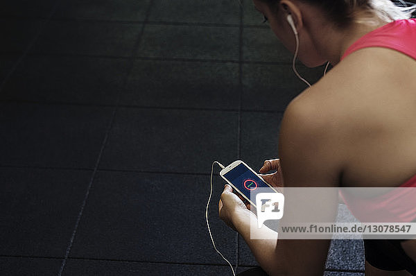 Hochwinkelansicht einer Sportlerin  die ein Smartphone im Fitnessstudio benutzt