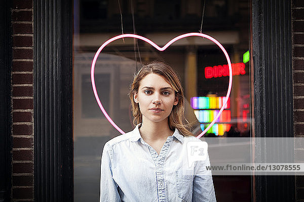 Porträt einer Frau  die vor beleuchteter herzförmiger Dekoration im Geschäft steht