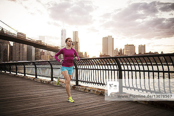 Frau joggt auf Promenade am East River in Stadt gegen Himmel
