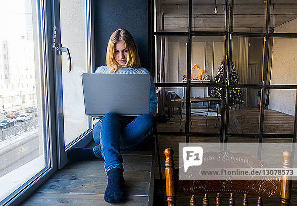 Teenagerin benutzt Laptop-Computer  während sie zu Hause am Fenster sitzt