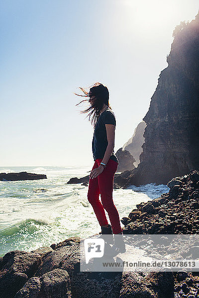 Frau steht auf Fels am Ufer gegen Meer und Himmel am sonnigen Tag