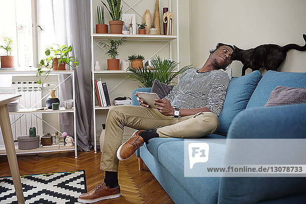 Man looking at cat while sitting on sofa in living room