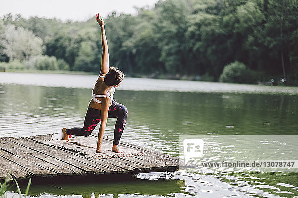 Frau praktiziert Yoga auf dem Pier über dem See im Wald