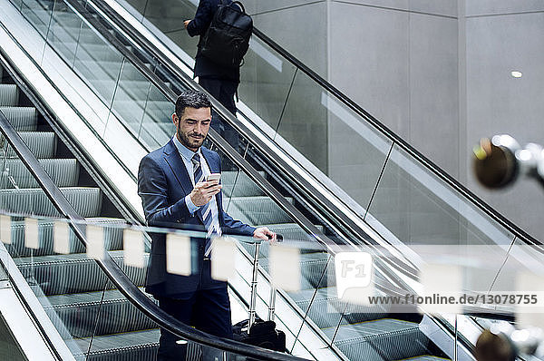 Geschäftsmann benutzt Smartphone auf Rolltreppe in U-Bahn-Station