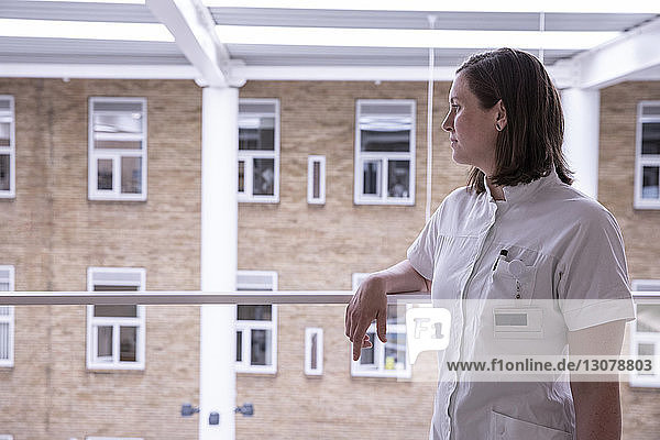 Thoughtful female doctor looking away while standing by railing in hospital
