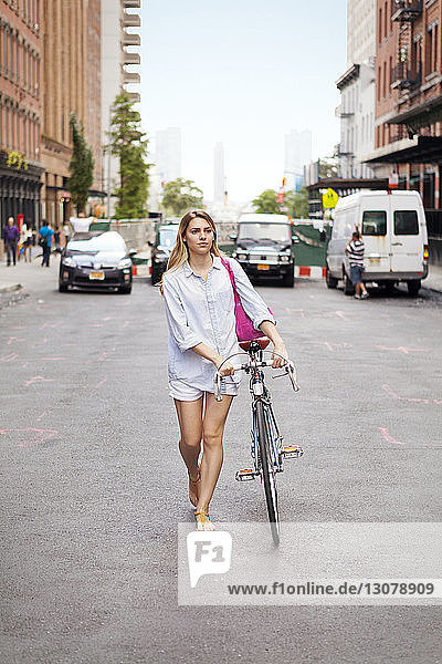 Frau zu Fuß mit Fahrrad auf der Straße in der Stadt