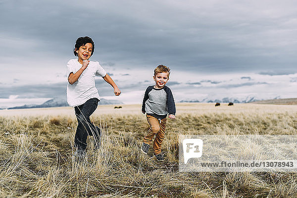 Brothers running while playing on grassy field against cloudy sky