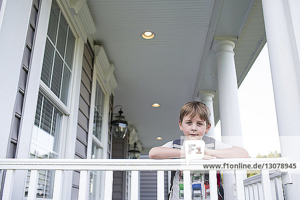 Portrait of boy with backpack standing by railing in patio
