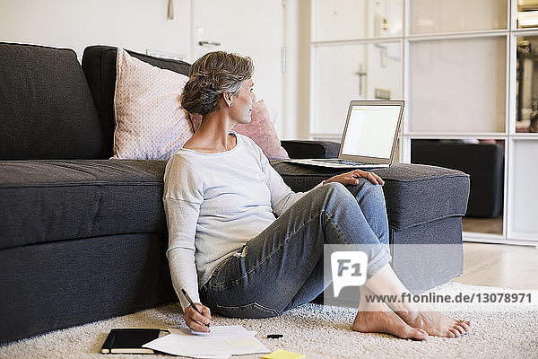 Mature woman writing while using laptop in living room
