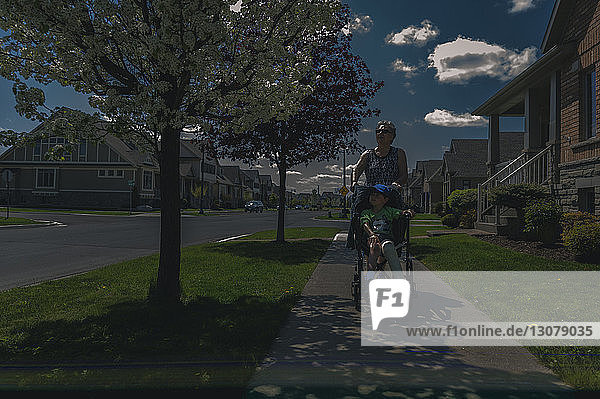 Grandmother pushing grandson on wheelchair on footpath
