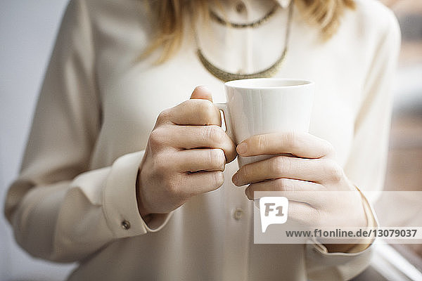 Midsection of businesswoman holding coffee cup in creative office
