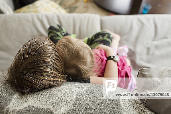High angle view of boy embracing sister while relaxing on sofa at home